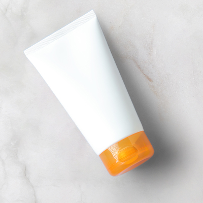 witte tube zonnebrandcrème met oranje dop op neutrale achtergrond